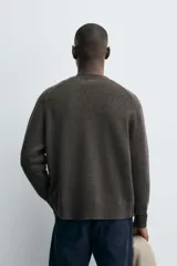 Cárdigan de punto en color verde oscuro, con cuello en pico, manga larga y cierre frontal con botones. Presenta acabados en rib en puños y bajo.