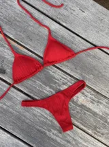 Conjunto de bikini rojo con textura, compuesto por un corpiño de triángulos movibles con tiras finas para atar al cuello y a la espalda, y una bombacha colaless con laterales fijos.