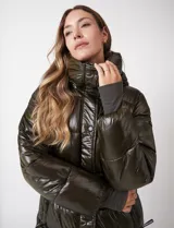 Campera puffer de acabado brillante, color verde oscuro, con cuello alto, cierre frontal con solapa de botones a presión, capucha desmontable y puños internos elastizados.
