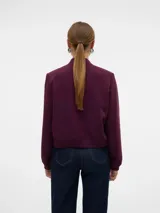 Campera bomber corta de color beige, confeccionada en tejido sarga, con cuello tipo rib, cierre frontal de botones a presión, bolsillos frontales con solapa y puños y dobladillo elasticados.