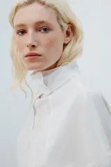 Camisa amplia blanca de cuello alto y manga larga, con cierre frontal de botones.