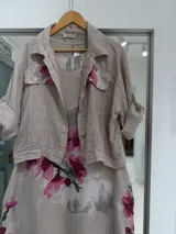 Set compuesto por una casaca y un vestido midi de lino color beige con estampado de grandes flores fucsias. La casaca es de mangas largas con puños arremangados y bolsillos frontales con solapa. El vestido es sin mangas, con corte midi y diseño fluido.