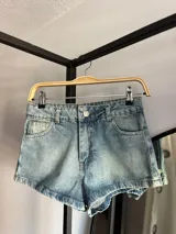 Short de jean celeste con lavado ácido, tiro alto, corte ajustado, bolsillos traseros con bordados y terminaciones desflecadas.