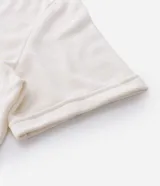 Remera de manga corta con cuello polo contrastante en azul marino y abertura en V. El cuerpo de la prenda es color crema y lleva un estampado frontal con la palabra "WONDER".