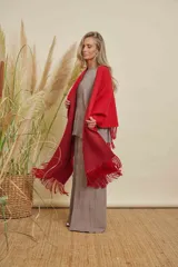 Ruana tejida color rojo, con terminación en flecos de lana y diseño en V en la espalda.