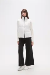 Chaleco acolchado blanco, sin mangas, con cuello alto y cierre frontal negro.