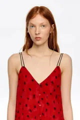 Vestido midi de corte recto con escote en V, tirantes dobles finos y cierre frontal con botones. Presenta un diseño estampado con manchas oscuras sobre fondo rojo.