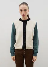 Saco de punto con diseño color block, cuello redondo y cierre frontal con botones. Presenta cuerpo en color crema, tapeta de botones en negro y mangas en color verde petróleo.