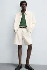 Bermuda de algodón color beige claro con rayas verticales finas en tono más oscuro. Diseño de corte regular con bolsillos delanteros y bolsillos traseros de plastrón.