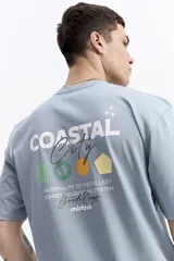 Remera de manga corta color celeste claro, con cuello redondo y estampado gráfico en la espalda que incluye texto y formas geométricas en blanco, verde, amarillo y naranja.