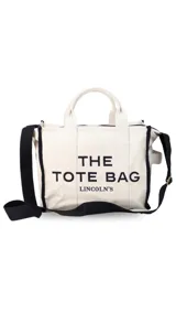 Bolso tipo tote bag de lona color beige con detalles de ribetes negros. Presenta el texto 'THE TOTE BAG' y 'LINCOLN'S' estampado en el frente. Cuenta con doble asa superior y correa ajustable extraíble.