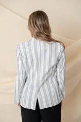Blazer blanco con rayas verticales negras, confeccionado en algodón y lino. Tiene tres bolsillos y cierre con botón de nácar.