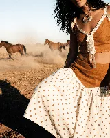 Falda midi de lino y algodón, color blanco roto con estampado de lunares marrones. Presenta un corte acampanado y un detalle de encaje blanco en la unión con la parte superior (que parece ser un top o parte de un conjunto).