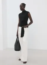 Top negro sin mangas con cuello perkins, detalle fruncido en la cintura y panel drapeado colgante en el frente.
