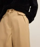 Bermuda color beige de corte recto confeccionada en tejido liso. Lleva una cinturilla transtemporal con dos botones y solapas plisadas justo debajo de la cintura.