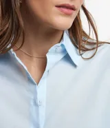 Camisa celeste de voile, corte oversized, con cuello clásico, cierre frontal con botones, mangas largas con puños largos y proceso de producción sostenible.