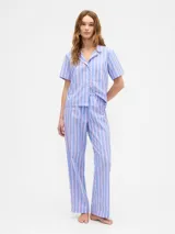 Pijama de dos piezas confeccionado en popelina, compuesto por una camisa de manga corta con cuello solapa y botones frontales, y un pantalón largo de corte recto con cintura elástica. Presenta un diseño de rayas verticales en tonos azul y rosado.