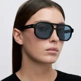 Lentes de sol estilo aviador con montura geométrica oversize en color negro y cristales polarizados en color azul. Presentan un diseño de doble puente con bordes biselados.