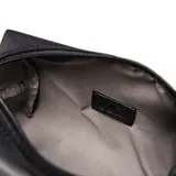 Portacosmético de diseño rectangular en color negro, confeccionado en material textil con acabado liso. Cuenta con una manija lateral para su transporte y un aplique metálico cuadrado con el logo de la marca en el centro.