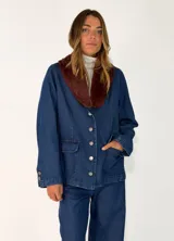 Chaqueta de denim azul con cuello de piel sintética en color marrón, cierre frontal con botones metálicos y bolsillos delanteros.