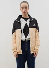 Campera de tela avión con diseño color block en negro y verde, con detalles de franjas blancas en las mangas. Presenta cierre frontal completo, cuello alto, puños y ruedo elásticos, y logo bordado en el pecho.