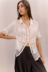 Camisa de algodón color crudo, con cuello camisero, mangas cortas y cierre frontal con botones. Presenta paneles de tejido calado y detalles bordados transparentes.
