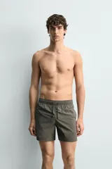 Bañador de hombre de largo medio, color celeste claro con rayas blancas horizontales. Presenta cintura elástica ajustable con cordón, bolsillos frontales y bolsillos traseros de plastrón. Incluye forro interior.