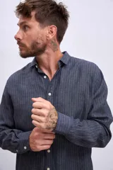 Camisa de manga larga para hombre, con cuello clásico y botones frontales. Presenta un estampado de rayas verticales finas en tonos azul claro y blanco.