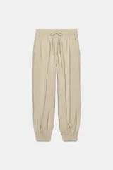 Pantalón satinado de tiro alto en color beige, con cintura elástica ajustable mediante cordones, bolsillos frontales y puños elásticos en los tobillos.