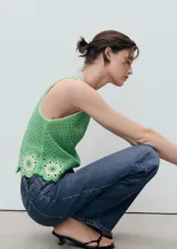 Top sin mangas verde de punto medio con cuello redondo y diseño recto. Presenta un detalle de bajo con acabado floral bordado y calado.
