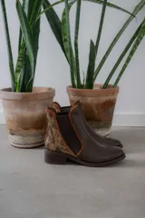 Botinetas de cuero color marrón con diseño tipo chelsea, con paneles laterales elásticos y detalle de cuero texturizado con acabado metalizado en el talón. Poseen taco bajo cuadrado y terminación redondeada.