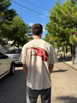 Remera de corte oversize color beige, con estampado gráfico abstracto en color rojo en la parte posterior.