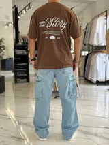 Remera oversize de manga corta color marrón con efecto gastado. Presenta inscripciones estampadas en color blanco en el frente y en la espalda.