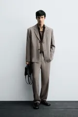 Pantalón de traje de corte slim fit, color marrón con textura sutil. Cuenta con cierre frontal de cremallera y botón, bolsillos laterales y bolsillos traseros de doble vivo con botón.