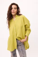 Camisa de corte oversize color verde lima, con cuello clásico, cierre frontal con botones y diseño de recortes diagonales en el frente. Posee mangas largas y un estilo holgado.