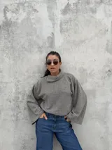 Polera de punto acanalado en color gris, con diseño de cuello abierto lateral, corte recto y mangas amplias.