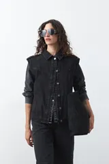 Chaleco de jean en tono celeste claro, con corte recto, cuello camisero, cierre frontal con botones metálicos y costuras visibles.