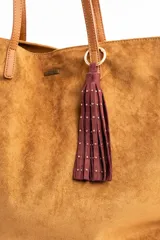 Charm para bolso compuesto por flecos de cuero sintético color marrón, decorados con pequeñas tachas metálicas doradas. Incluye un aro y un cierre de mosquetón metálico en tono dorado.