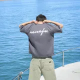 Remera gris de algodón, corte oversize, con mangas cortas y estampado en la espalda con la palabra 'nenefa' en cursiva blanca.