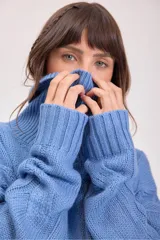 Sweater de punto color azul, con cuello alto y diseño de trenzas verticales. Presenta mangas largas con puños acanalados y un corte holgado.