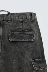 Pantalón cargo de denim lavado negro, corte relajado y tiro medio. Presenta múltiples bolsillos cargo con solapa y detalle de cierre en las perneras, además de bolsillos de vivo traseros. El bajo es ajustable con trabilla.