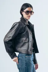 Chaqueta de cuero sintético en color marrón oscuro, con cuello clásico, cierre frontal con botones a presión y dos bolsillos aplicados en el pecho. Presenta un corte recto y estructurado.