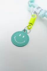 Llavero de cordón rosa con nudo, herrajes plásticos, gancho mosquetón y dije circular con cara feliz.