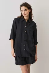 Camisa negra de manga corta, con cuello camisero, cierre frontal de botones y un bolsillo aplicado en el pecho.