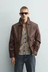 Sobrecamisa de corte relajado confeccionada en tejido efecto piel color marrón. Presenta cuello solapa, cierre frontal con cremallera, mangas largas con puños abotonados y dos bolsillos de plastrón con solapa en la parte frontal.