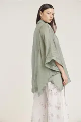 Camisa de manga ancha, color verde salvia, con cuello camisero y cierre frontal de botones. Presenta detalles de pespunte decorativo en el canesú frontal.