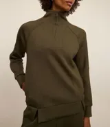 Buzo deportivo verde oliva de microfibra pesada, con cuello alto con cremallera, recorte en los hombros y dos aberturas en la parte de abajo.