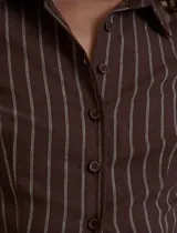 Camisa de manga larga color marrón oscuro con finas rayas verticales blancas. Presenta un corte entallado y ligeramente cropped, con cuello camisero y cierre frontal de botones.