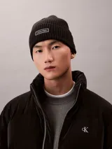 Gorro tipo beanie de punto grueso acanalado en color negro, con vuelta y parche rectangular con el logo de Calvin Klein en el frente.