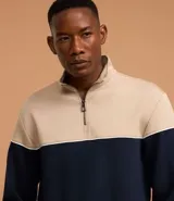 Buzo de media malla con diseño de bloques de color, presentando la parte superior en beige y la inferior en azul marino, separadas por una línea blanca. Cuenta con cuello alto con cierre frontal parcial y puños acanalados.